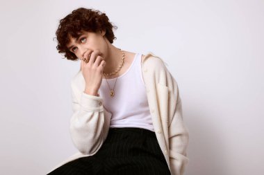 Yakışıklı genç adam düşünceli bir şekilde oturur, sade bir arka plana karşı şık bir kıyafet sergiler..