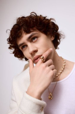 Yakışıklı genç adam şık kıyafetler ve çarpıcı mücevherler sergilerken düşünceli bir şekilde poz veriyor..