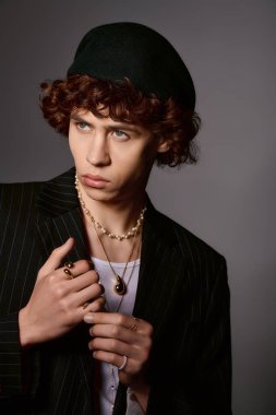 Şık giyinmiş kendine güvenen genç adam, tarafsız bir arkaplana karşı çarpıcı bir ifadeyle poz veriyor..