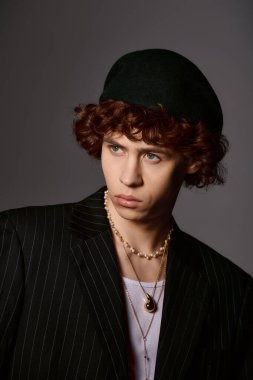 Yakışıklı genç adam şık bir bere ve takının bulunduğu modaya uygun bir kıyafetle güven içinde poz veriyor..