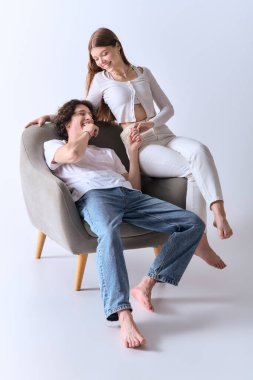 Neşeli genç çift şık bir sandalyede oturuyor, gri bir stüdyoda gülüşlerini ve aşklarını paylaşıyorlar..