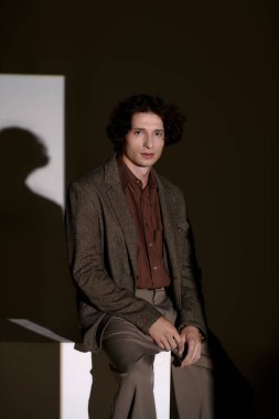 Tarz sahibi genç bir adam, gri bir arkaplan karşısında şık bir elbiseyle rahatça poz verir..