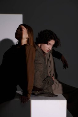 Genç çift şık kıyafetler içinde, koyu gri bir stüdyoda birbirlerinin tarzlarını kucaklıyor..