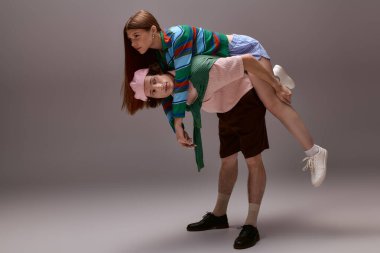 Modaya uygun genç bir çift, gri bir stüdyoda neşe içinde poz verirken tarzlarını sergiliyor..