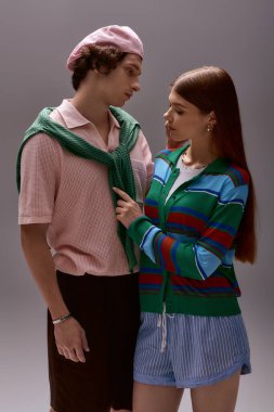 Şık bir çift, eşşiz tarzlarını moda kıyafetleriyle gri bir stüdyo arkaplanına karşı ifade ediyor..