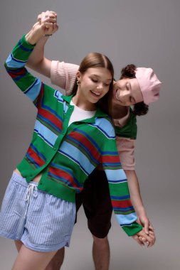 Modaya uygun bir çift, şık kıyafetler giyerken koyu gri bir stüdyoda neşe içinde poz veriyor..