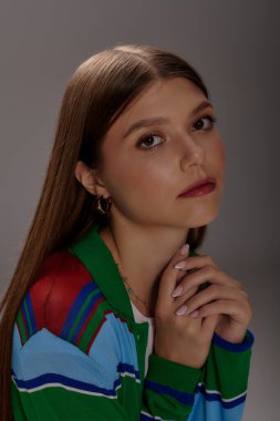 Tarz sahibi genç bir kadın, gri bir stüdyo arkaplanına karşı şık bir kıyafetle güven içinde poz veriyor..