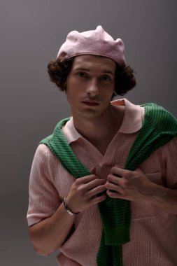 Genç bir adam minimalist gri bir stüdyoda kendine güvenen şık bir kıyafetle poz veriyor..