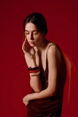 Dalgalı elbiseli bir kadın düşünceli, sakin bir bakışla yüzüne dokunuyor..