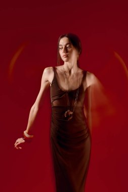 Şık bir kadın şık bir elbiseye güvenir, canlı kırmızı renge karşı zarif pozlar verir..