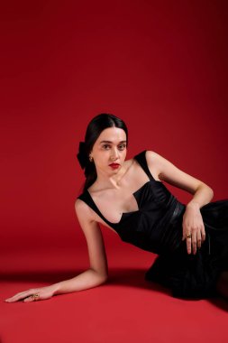 Beautiful woman with long hair lies on the ground, showcasing her stunning outfit and makeup.