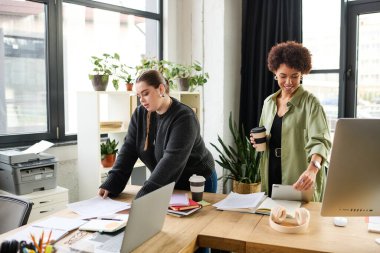 İki kadın, canlı bir kurumsal ortamda takım çalışması yapar, fikirleri paylaşır..