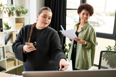 İki genç kadın parlak bir ofiste birlikte çalışıyor, fikirleri ve belgeleri paylaşıyorlar..