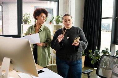 Genç ve cüsseli kadın canlı bir ofiste Afrikalı Amerikalı meslektaşıyla fikirleri tartışıyor..
