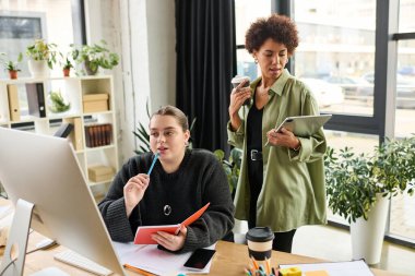 İki kadın yönetici, yeşillik ve ışıkla dolu modern bir ofiste bir projeyi tartışıyor..