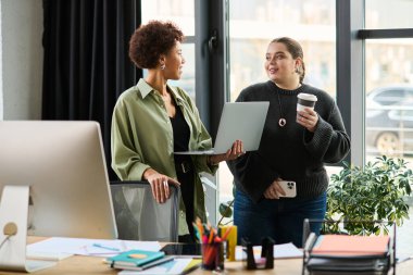 İki kadın yönetici parlak bir ofiste kahve içerken fikirleri tartışıyor..