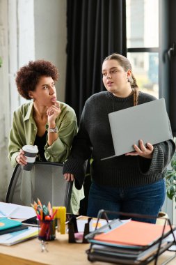 Genç ve cüsseli kadın, canlı bir ofiste Afrikalı Amerikalı meslektaşıyla fikirlerini paylaşıyor..