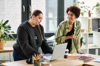 Büyük beden bir kadın dizüstü bilgisayarında çalışırken gülümseyen siyahi meslektaşı takım çalışması yapıyor..