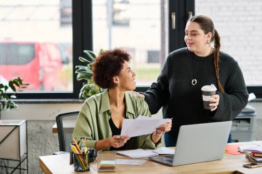 Genç ve cüsseli kadın ve Afrikalı Amerikalı meslektaşı iş yerinde sohbet ediyorlar..
