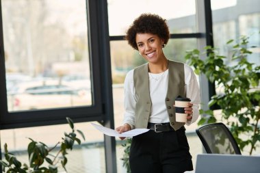 Parlak bir ofiste çalışırken elinde gazete ve kahve tutan siyah bir kadın..