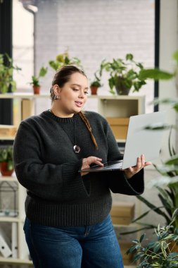 Geniş beden bir bayan yönetici, canlı ofis bitkileri arasında dizüstü bilgisayarı üzerinde dikkatle çalışır..