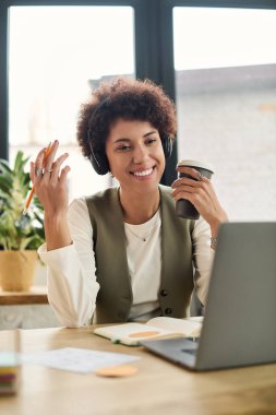 Parlak bir ofiste, genç bir Afrikalı Amerikalı iş kadını bir video görüşmesi sırasında gülümsüyor..