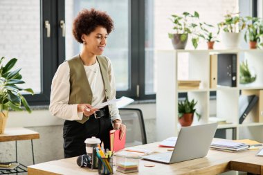 Genç bir Afrikalı Amerikalı iş kadını bilgisayarını parlak bir ofis ortamında kullanırken gülümsüyor..