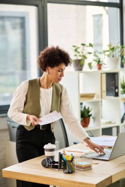 Şık bir ofiste görevleri yönetirken dizüstü bilgisayarıyla meşgul olan odaklanmış genç bir profesyonel..