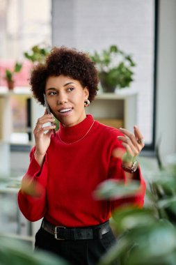 Genç bir iş kadını canlı bir ofiste yeşilliklerle çevriliyken telefonda konuşuyor..