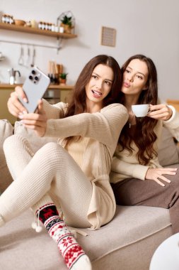 İkiz kardeşler sıcak bir oturma odasında selfie çekerken kahkahalarını paylaşıyorlar..