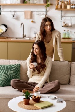 İkiz kardeşler kahkahalarını ve sıcak bardağını bitkilerle dolu parlak bir mutfakta paylaşırlar..