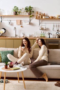 İki neşeli ikiz kardeş şık bir oturma odasında rahatlar, sıcak içkileri paylaşır ve gülümserler..