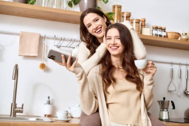 İkiz kız kardeşler, güzel tasarlanmış mutfaklarında rahatlarken gülücüklerini paylaşırlar, içkilerini yudumlarlar..