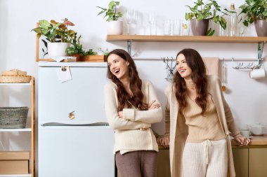 İkiz kardeşler, yeşil ve arkadaşlıkla çevrili sıcak, davetkar bir mutfakta birlikte gülerler..