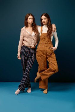 Genç ikiz kardeşler dikkat çekici bir mavi arkaplan karşısında zarif bir şekilde dururlar..