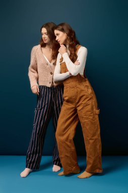 Genç ikiz kardeşler birlikte poz verir, modaya uygun kıyafetlerle mutluluk ve tarz gösterirler..
