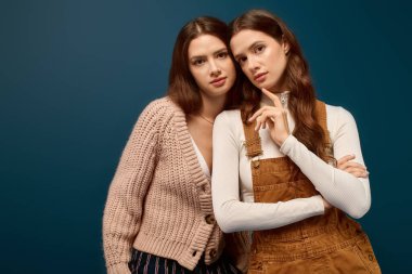 İkiz kardeşler düşünceli bir şekilde poz verir, benzersiz tarzlarını sergilerler ve huzurlu bir ortamda birbirlerine yakın dururlar..