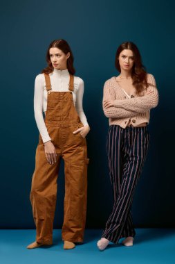 İki genç ikiz kardeş şık kıyafetler içinde canlı bir arkaplanda poz veriyorlar..