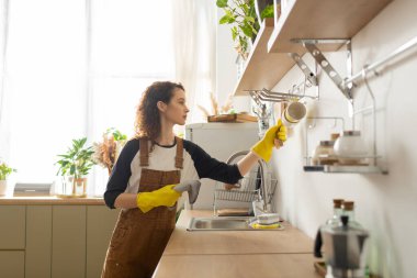 Kıvırcık saçlı kadın modern mutfağını düzenliyor, temizlik sürecinin tadını çıkarıyor..