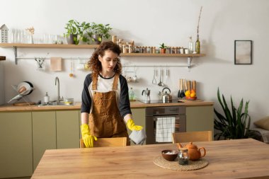 Kıvırcık saçlı kıvırcık bir kadın modern dairesini temizliyor, günlük tarzını sergiliyor..