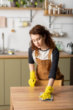 Kıvırcık saçlı genç bir kadın şık dairesini temizliyor..