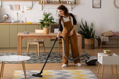 Bukleli neşeli genç bir kadın modern dairesini temizlerken anın tadını çıkarıyor..