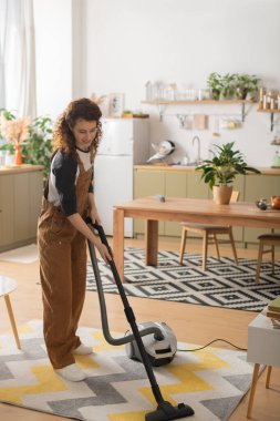 Gündelik giysiler içindeki neşeli genç kadın şık dairesini süpürüyor, temiz bir yer yaratıyor..