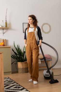 Gündelik giysiler içindeki genç bir kadın şık dairesini temizliyor, rahat bir ortam yaratıyor..