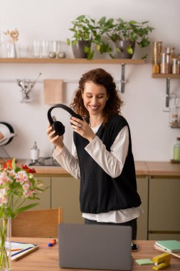 Şık evinde müzik dinlerken kıvırcık saçlı genç bir kadın gülümsüyor..