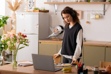 Curly-haired woman in casual attire focuses on her work while surrounded by vibrant decor.