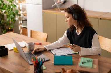 Kıvırcık elbiseli genç bir kadın rahat masasında dizüstü bilgisayarını kullanıyor..