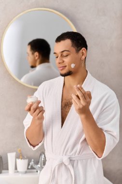 Genç adam rahat bir banyoda cilt bakım anlarından zevk alıyor, neşeyle cilt ürünlerini keşfediyor..