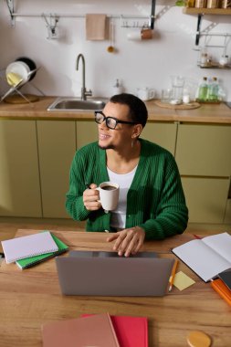 Yakışıklı adam mutfak masasında kahvesini yudumlarken gülümsüyor, işine dalmış..