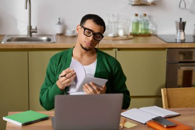 Genç bir adam elinde bir defter tutarken, rahat bir ev ortamında düşünür..